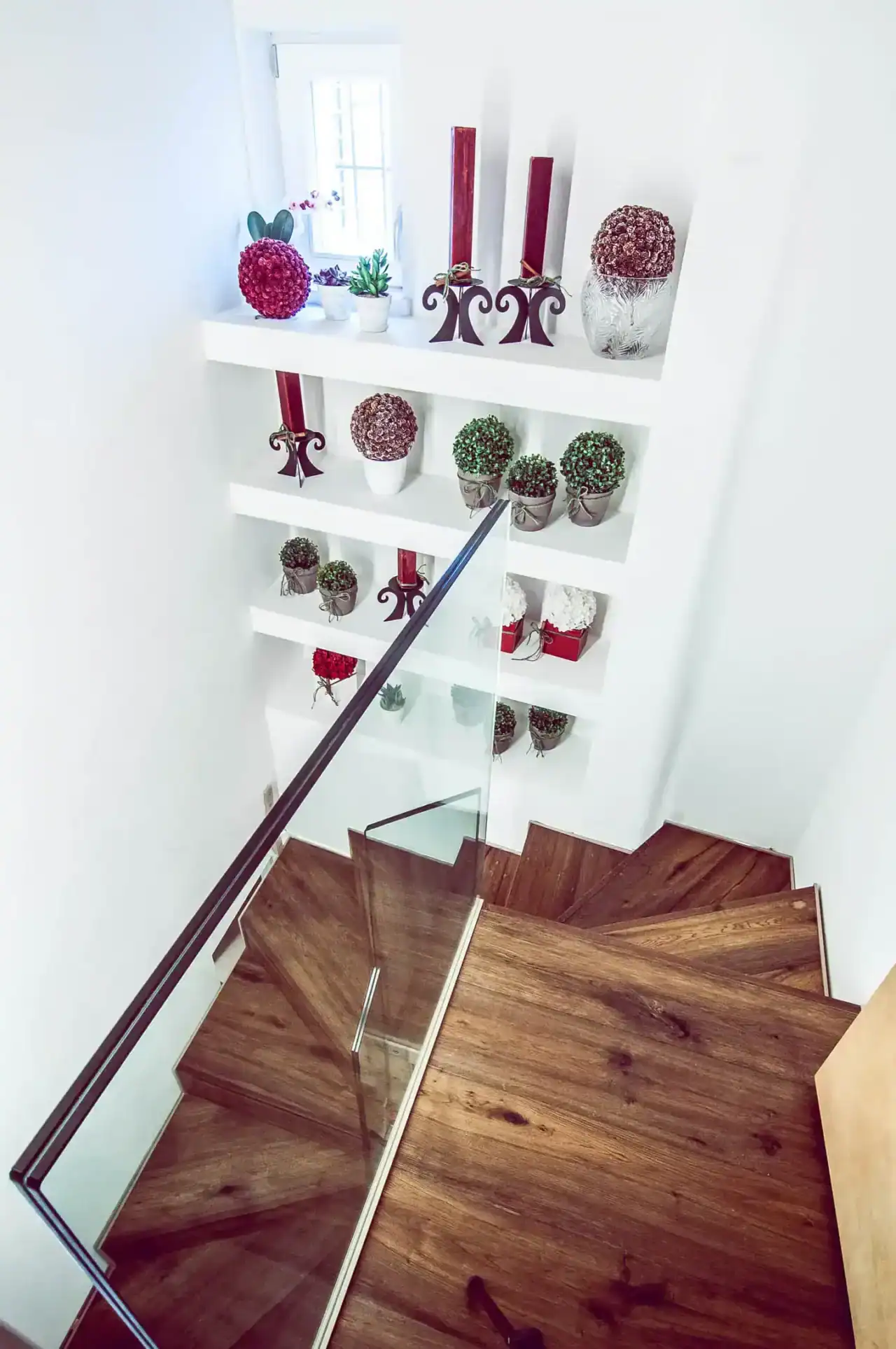 Decorazioni natalizie con piante e candele rosse su mensola bianca.